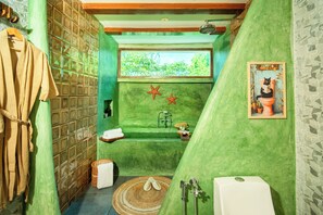 Une salle de bain avec un mur vert, une baignoire, une douche et une fenêtre donnant sur des arbres.