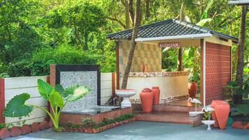 A small, traditional-style structure with a tiled roof, a sign reading 'ATITYAM', and a water feature in front.