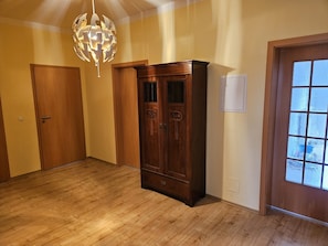 Ein Zimmer mit Holzboden, einem großen Holzkasten, einer Tür mit gefrosteten Glasfeldern und einer hängenden Leuchte.