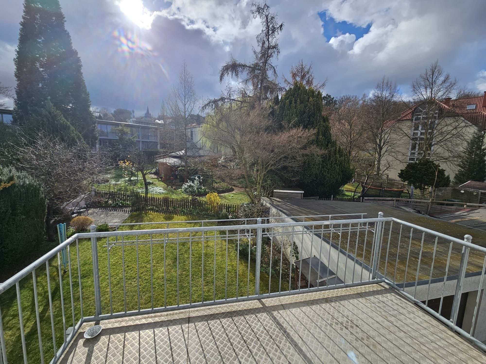 A metal staircase with a textured floor leading to a grassy area with trees and a building in the background.