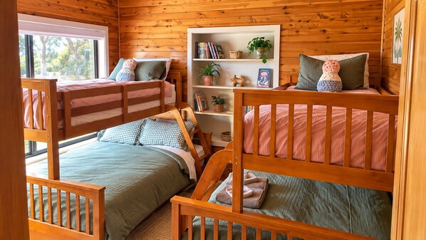 A cabin-style bedroom with bunk beds, a bookshelf, and a window with a view of trees.