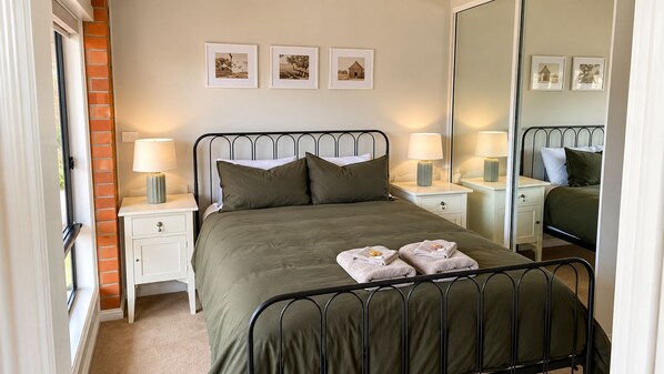 A neatly made bed with two pillows, a bedside table with a lamp, and a mirror on the wall.