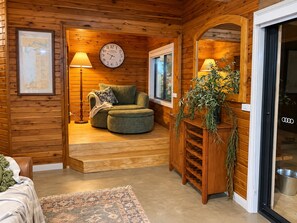 A cozy room with a wooden interior, a green armchair, a wall clock, and a plant.