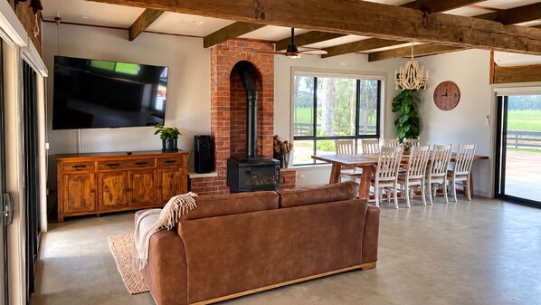 A spacious living area with a leather sofa, wooden dining table, and a brick fireplace.