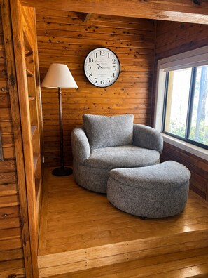 A cozy room with a wooden interior, a round armchair, a floor lamp, and a large wall clock.