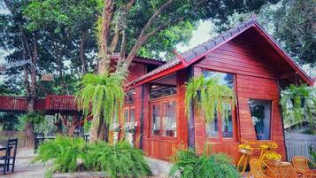 A wooden cabin with a sloped roof, surrounded by lush greenery and ferns.