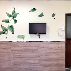 A reception desk with a flat-screen TV, a wall-mounted telephone, and a decorative wall with leaf and bird decals. - Royal Paris Guesthouse (Kowloon)
