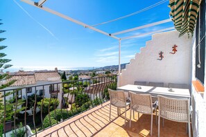 Ein Balkon mit Tisch und Stühlen, der auf eine Stadtansicht mit Gebäuden und blauem Himmel blickt.