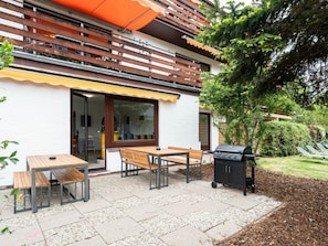 Eine Terrasse im Freien mit Grill, Holztischen und Stühlen.