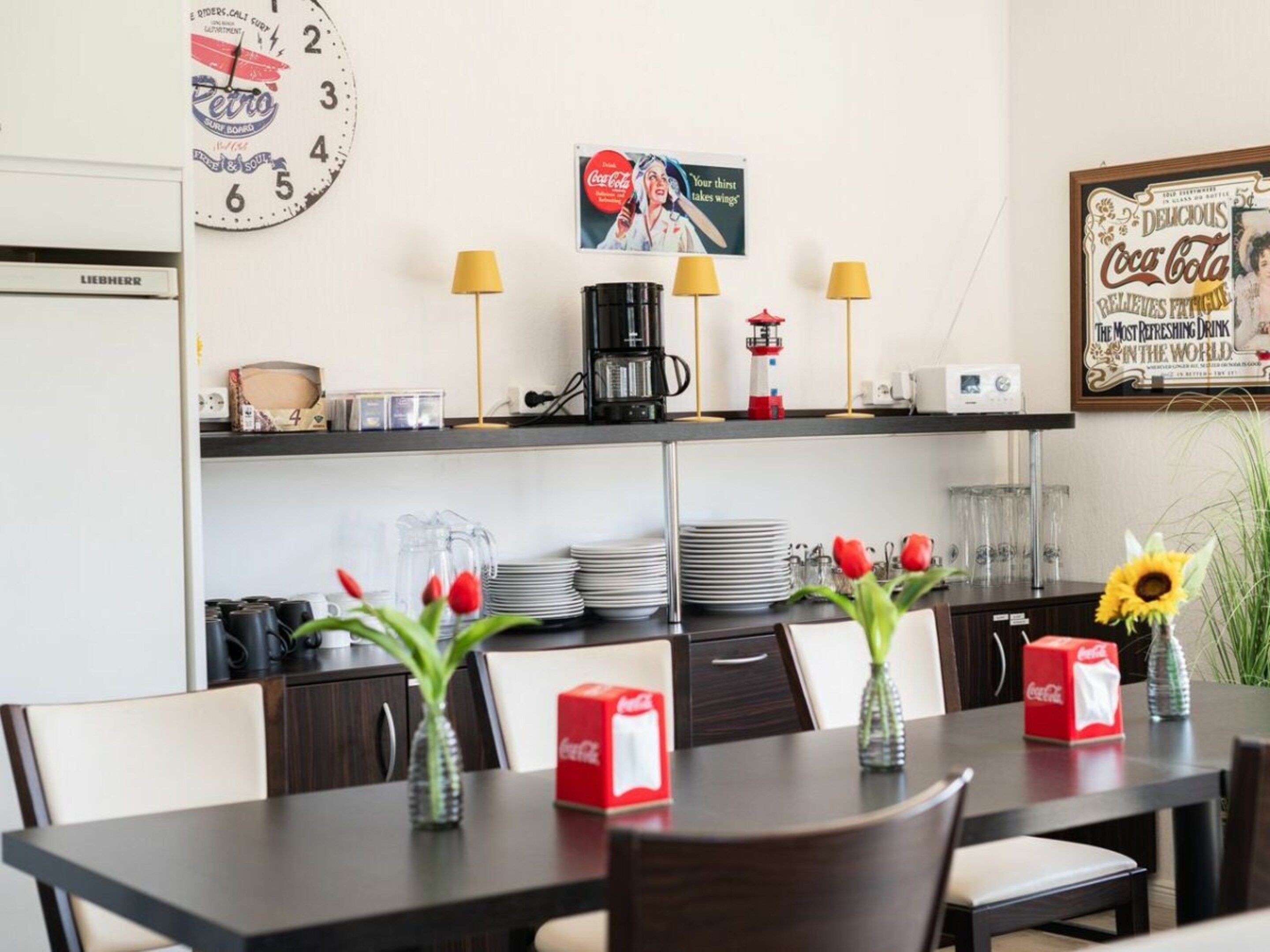 A dining area with a table set for two, a coffee machine, and a clock on the wall.