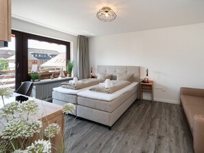 Ein modernes Schlafzimmer mit einem Doppelbett, einem Nachttisch, einer Lampe und Blick ins Freie.