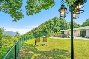 A fenced outdoor area with chairs and a table, a building with a green roof, and a mountain in the background. - Early Blue Motel (Saluda)