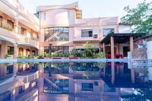 Un hotel de diverses plantes amb una piscina reflectant, balcons i plantes d'interior.