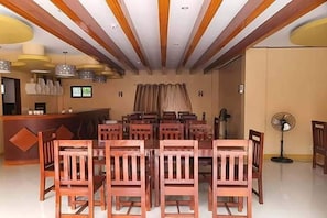 Zona de menjador amb taules i cadires de fusta, una recepció i llums penjants.