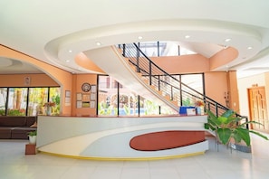 Un vestíbul modern amb una recepció corbada, unes escales i vista cap a l'exterior.