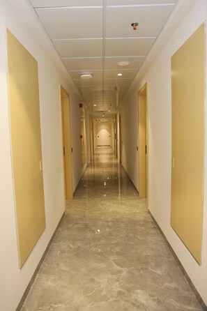 A corridor with doors on both sides, a shiny floor, and a ceiling with recessed lighting. - Varay Prime (Ujjain)