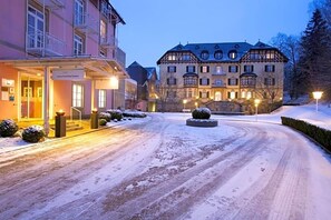 Hotel com arquitetura europeia tradicional, rampa de acesso coberta de neve e entrada bem iluminada.