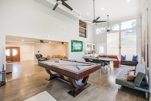 A spacious living area with a pool table, a sofa, and a dining table. There are ceiling fans and a large window providing natural light. - Experience resort style luxury at the stylish Houston property with a private pool. Minutes from the city's top dining and shopping. (Houston)