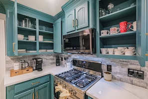 A kitchen with teal cabinetry, a stainless steel microwave, and a gas stove. - Experience resort style luxury at the stylish Houston property with a private pool. Minutes from the city's top dining and shopping. (Houston)