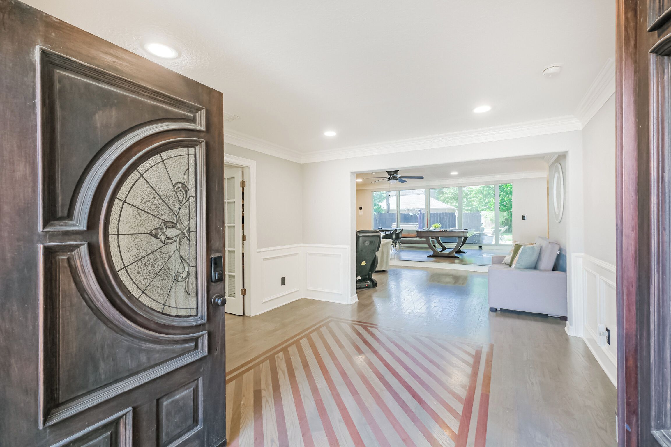 Un recibidor amplio con una puerta de madera grande, un área de comedor con mesa de billar y una sala de estar con sofá.