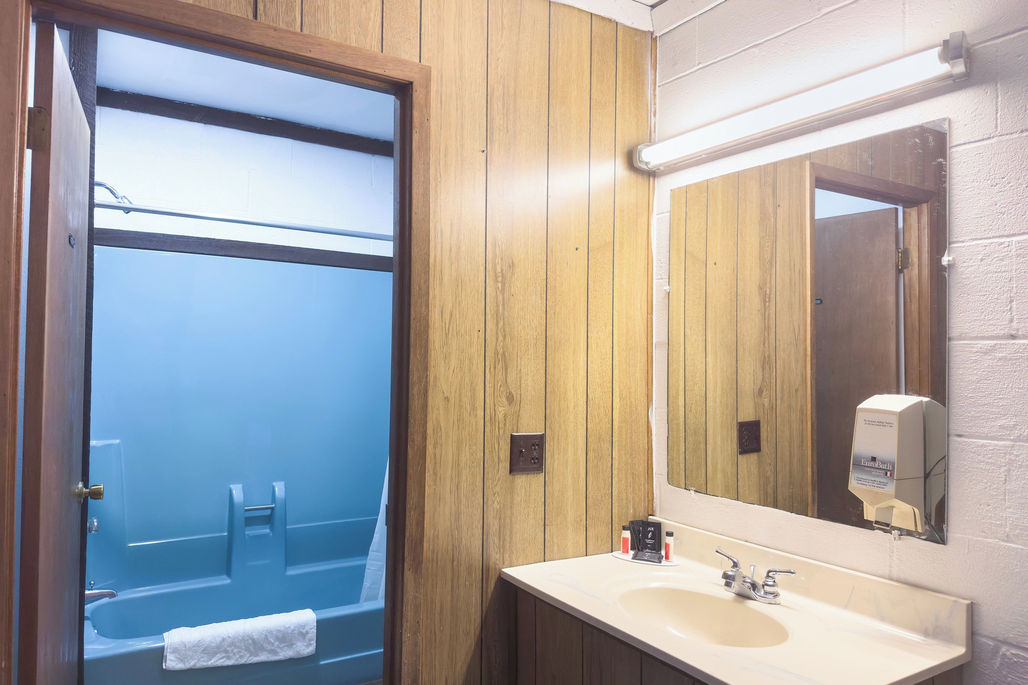 A bathroom with a wooden panel wall, a mirror, a sink, and a towel hanging on the door.