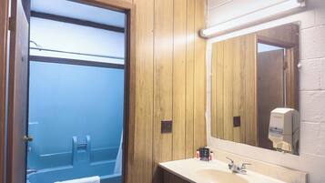 A bathroom with a wooden panel wall, a mirror, a sink, and a towel hanging on the door.