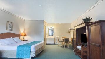 A hotel room with a bed, bedside lamp, a desk with a chair, a television, and a wardrobe.