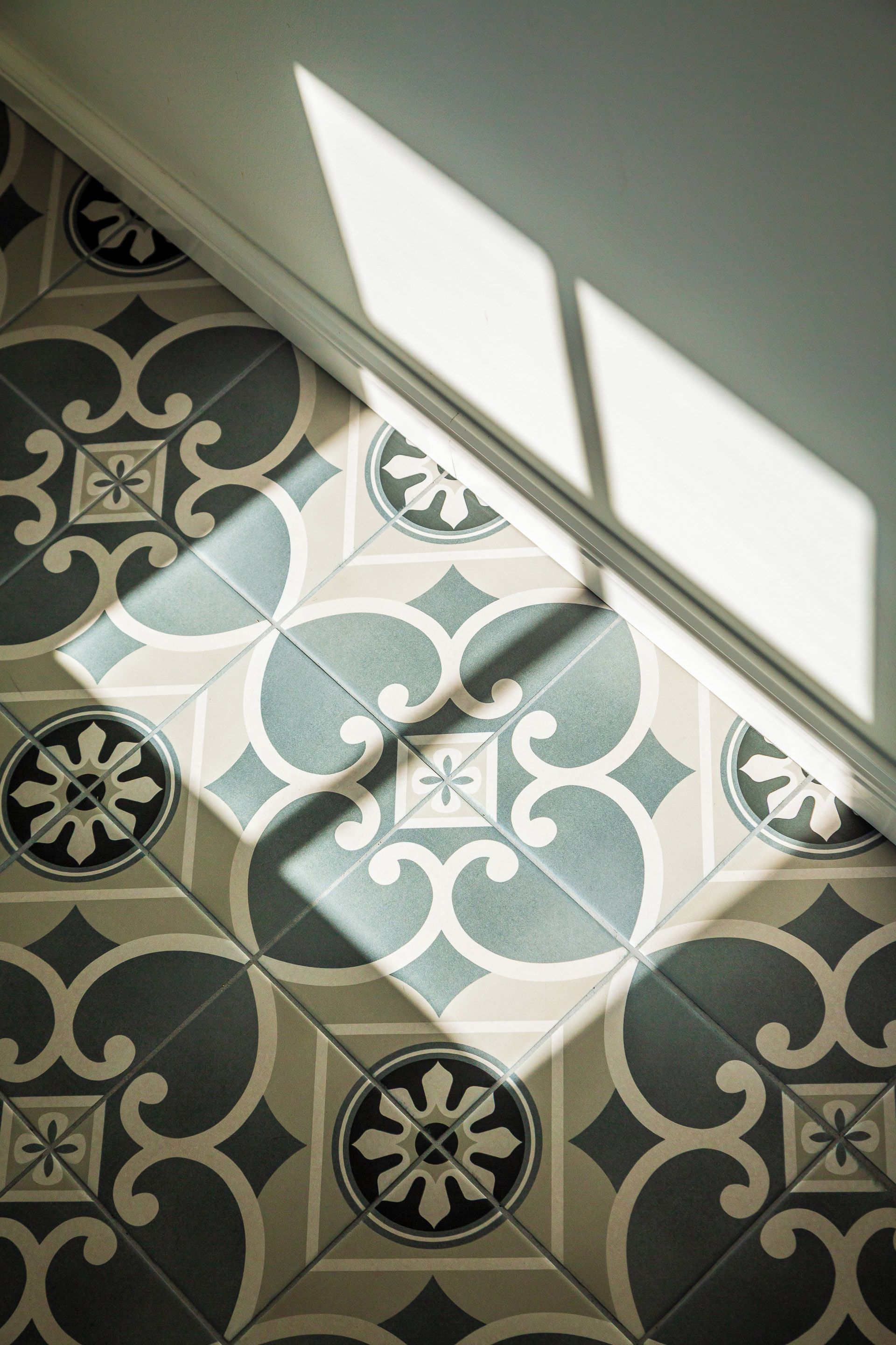 A patterned floor with a geometric design, a white wall, and a shadow cast by a window.