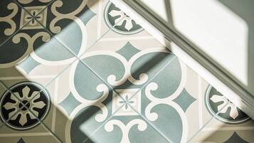 A patterned floor with a geometric design, a white wall, and a shadow cast by a window.