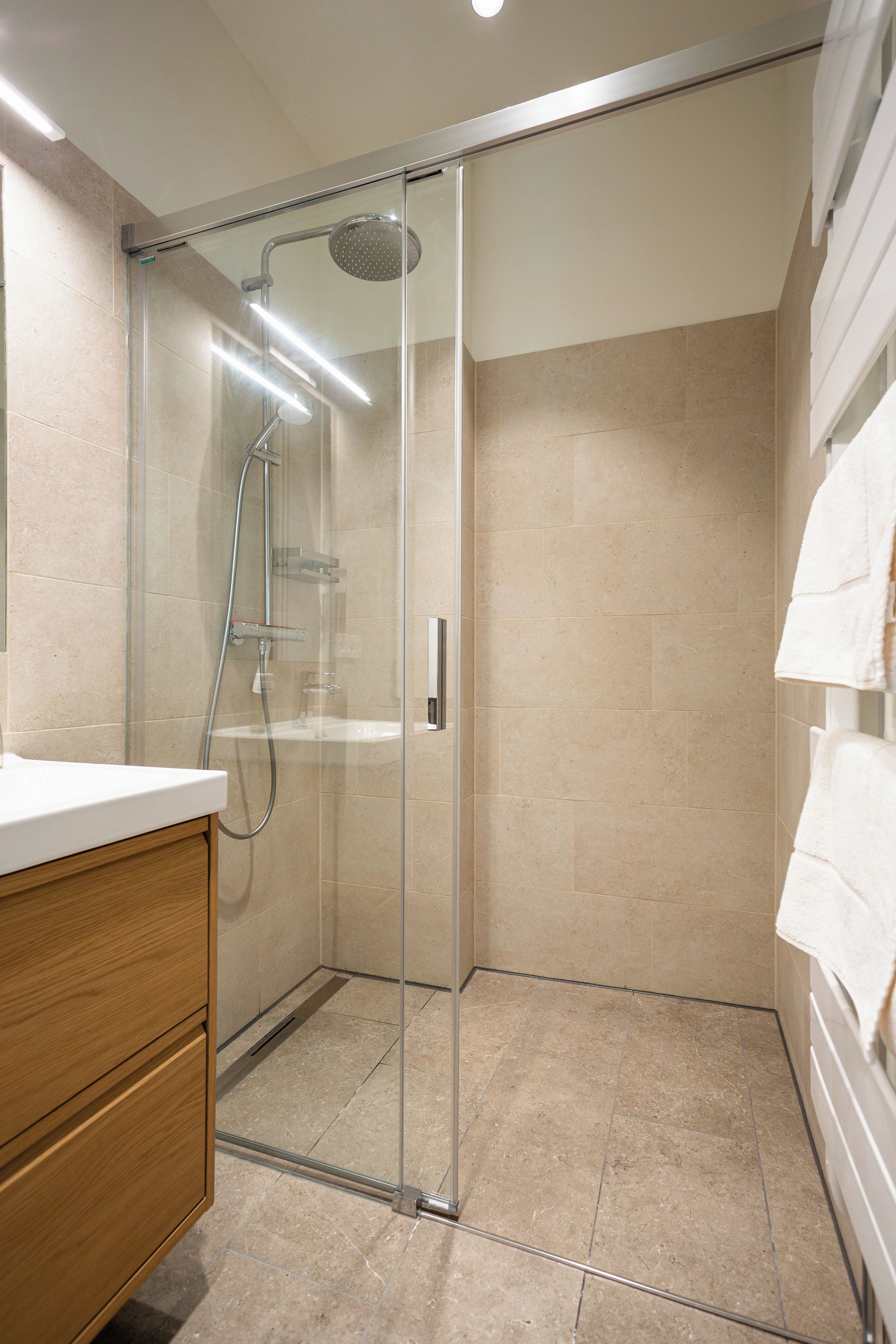 Une salle de bain moderne avec une douche à parois de verre, un meuble-lavabo en bois et un porte-serviettes blanc.