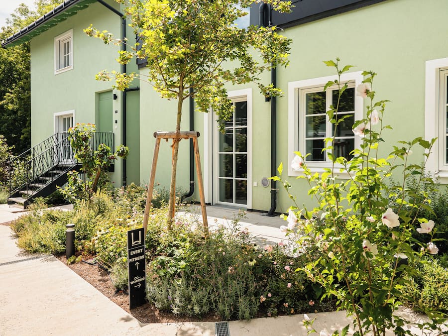 A green building with a garden in front, a wooden swing, and a sign for a fitness center.