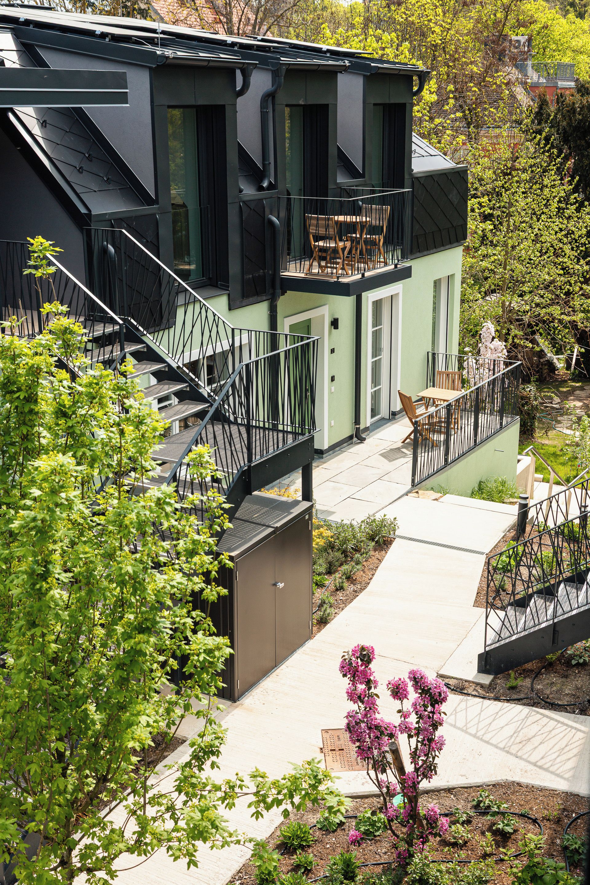 A two-story building with a balcony, a staircase, and a garden area.