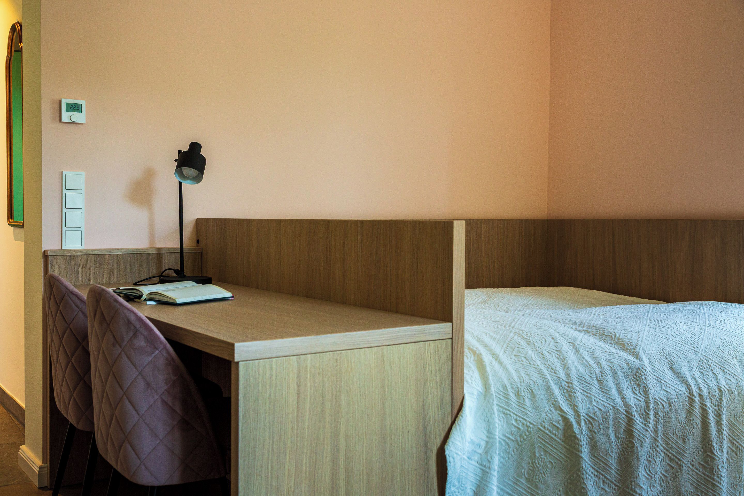Une chambre à coucher avec un bureau en bois, deux chaises, une lampe et un lit recouvert d’une couvre-lit à motifs.