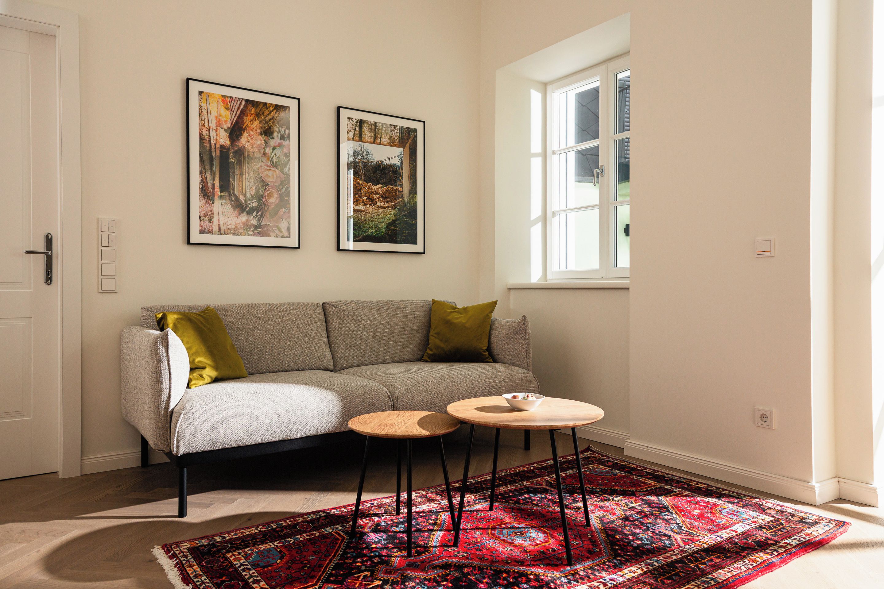 A room with a sofa, a small round table, a patterned rug, and two framed pictures on the wall.