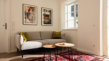 A room with a sofa, a small round table, a patterned rug, and two framed pictures on the wall.