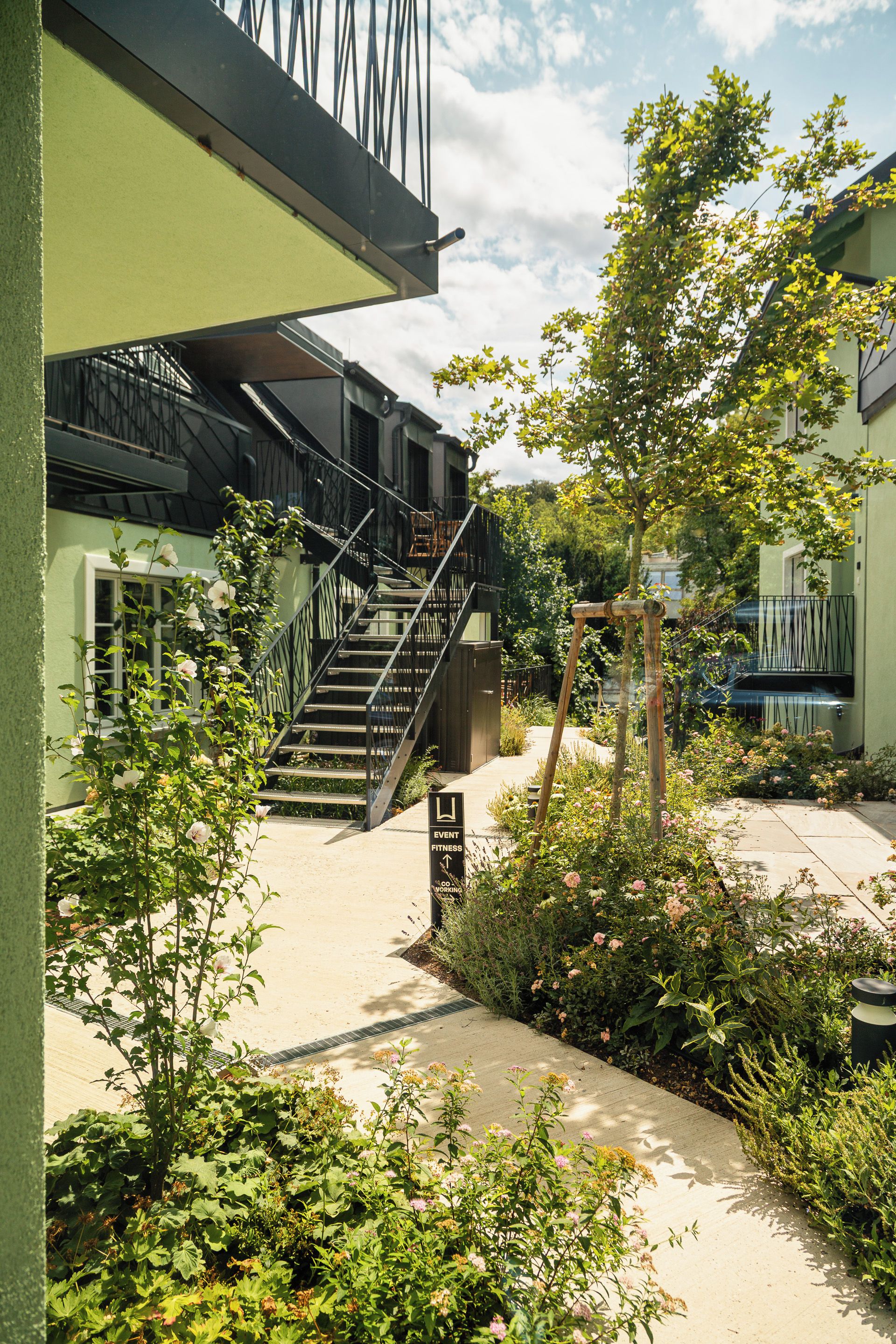 Un patio con una escalera que lleva a un edificio, rodeado de follaje y flores.