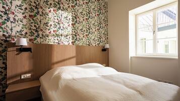 A bedroom with a bed, a window, and a wall with a floral pattern.