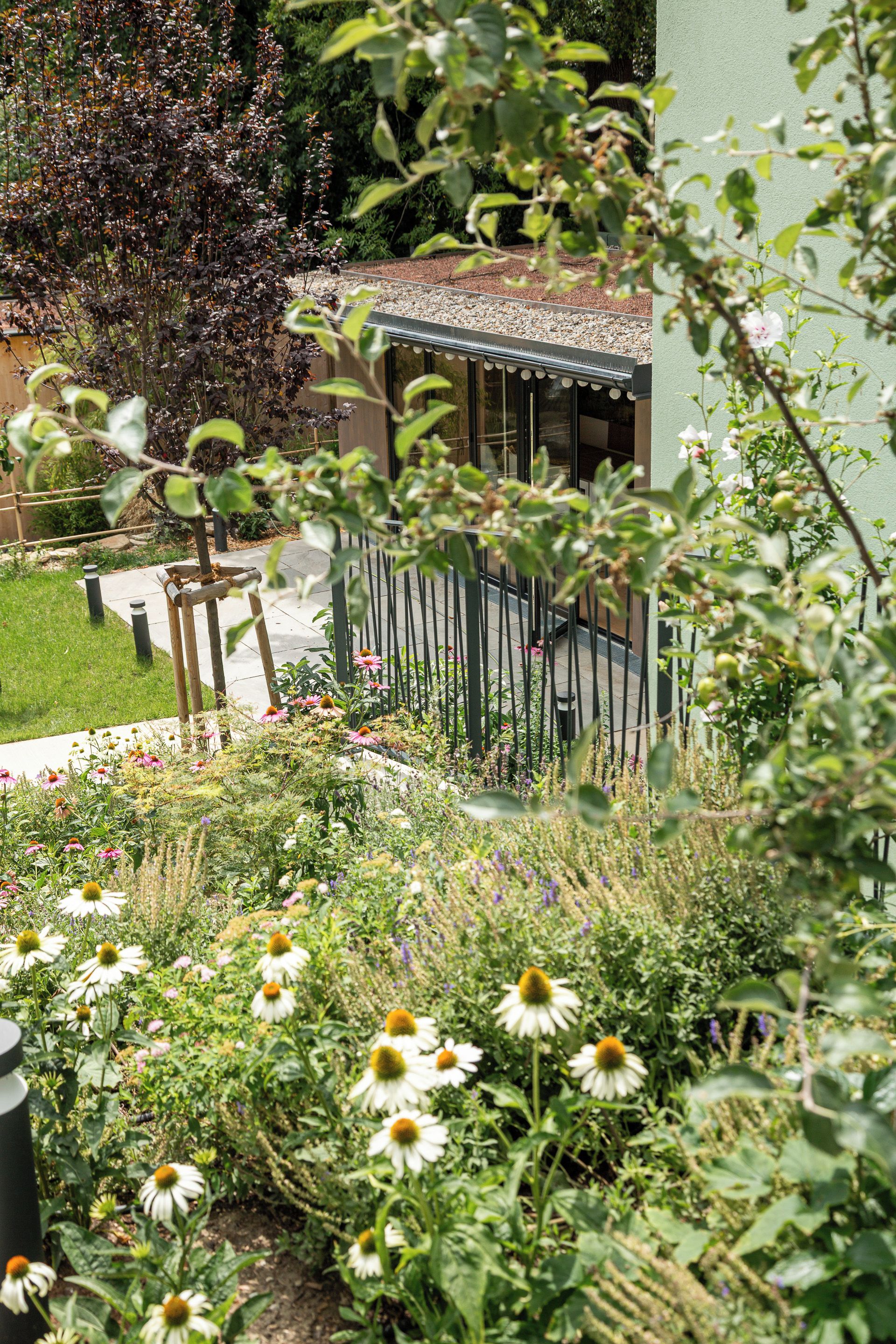 Ein Garten mit verschiedenen Blumen und Pflanzen, einem Holzzaun und einem Gebäude mit schrägem Dach.