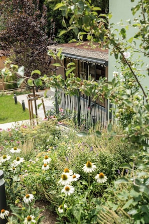 A garden with a variety of flowers and plants, a wooden fence, and a building with a sloped roof.