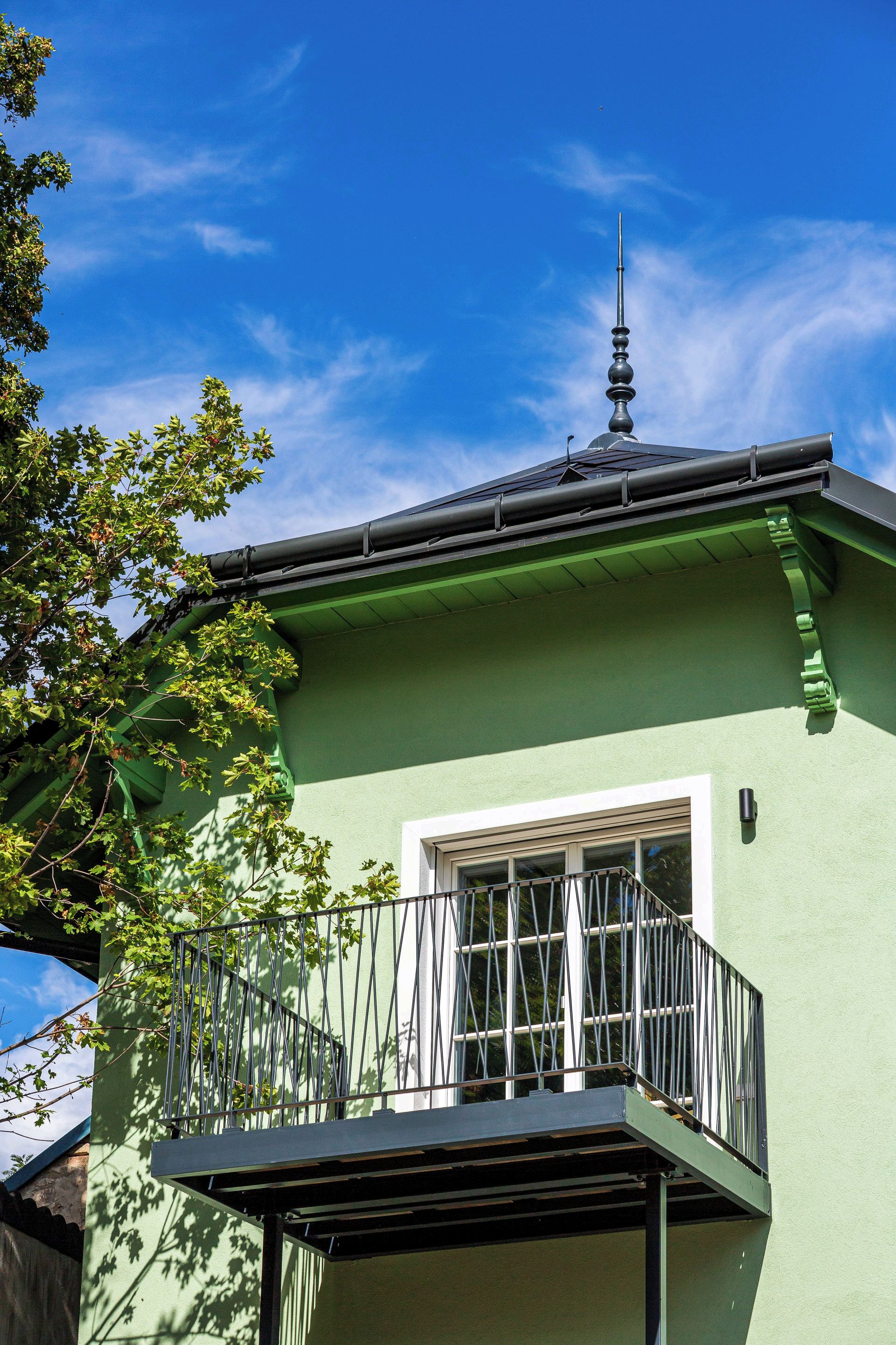 A green building with a balcony, a window, and a chimney.