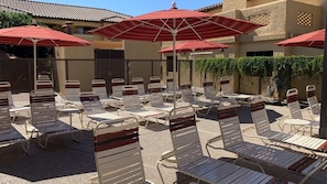 A sunlit outdoor seating area with metal chairs and red umbrellas, surrounded by a building with a tiled roof. - Your Desert Oasis Awaits at Holiday Inn Club Vacations Scottsdale Resort- 2 Bd. (Scottsdale)