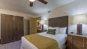 Habitación de hotel con una cama grande, un armario, una mesita de noche con lámpara y un ventilador de techo.