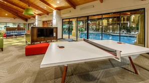 Un área interior de piscina moderna con mesa de ping pong, asientos y una gran pantalla de televisión.