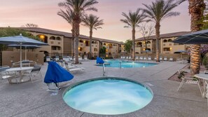 A pool area with lounge chairs and umbrellas, surrounded by palm trees and a building with arched windows. - Your Desert Oasis Awaits at Holiday Inn Club Vacations Scottsdale Resort- 2 Bd. (Scottsdale)
