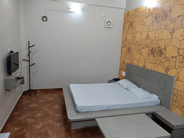 Un lit simple avec une tête de lit, une table de chevet, un téléviseur fixé au mur et un porte-manteau.