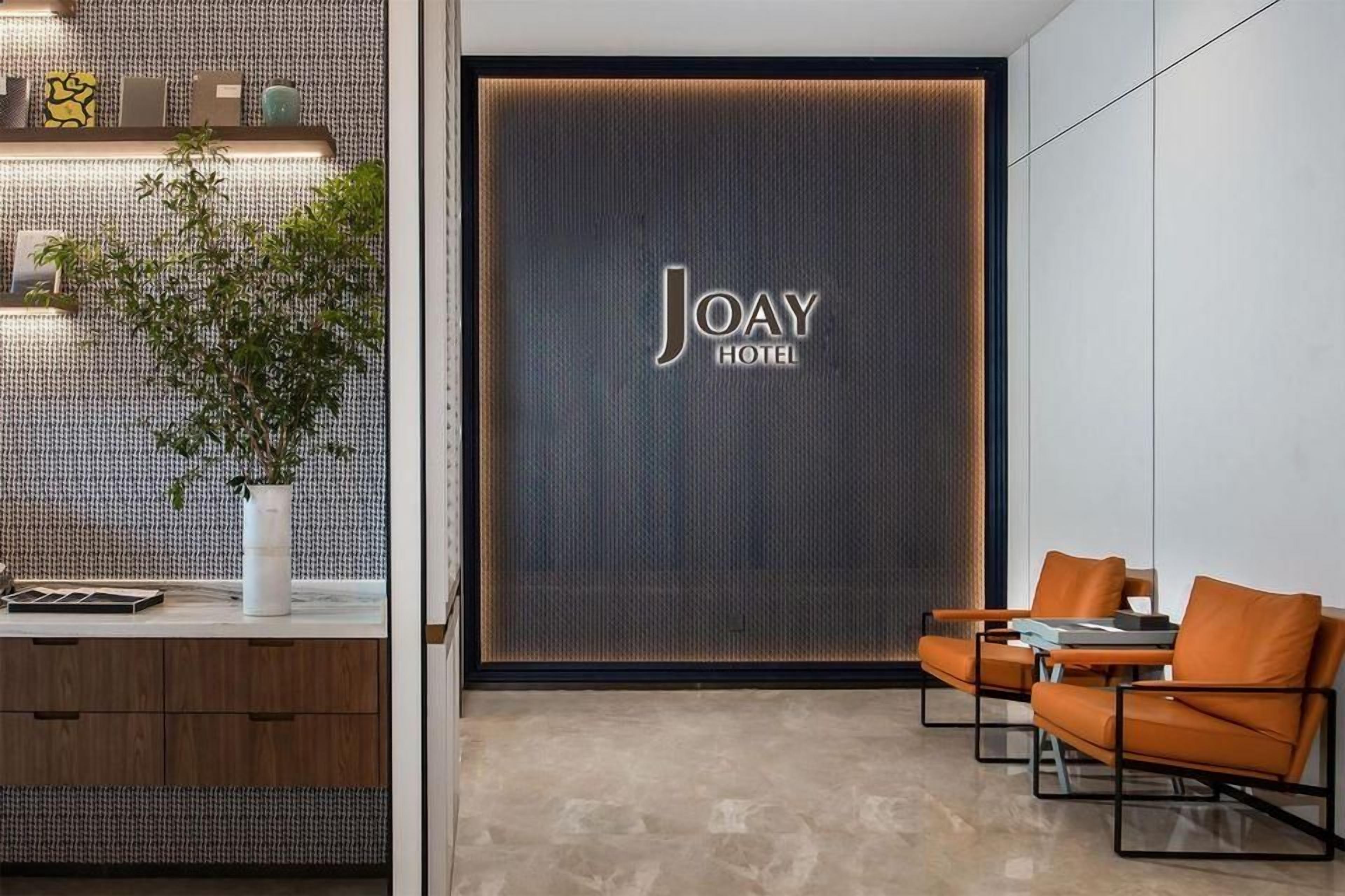 A modern hotel lobby with a reception desk, seating area, and a large wall with the hotel name.