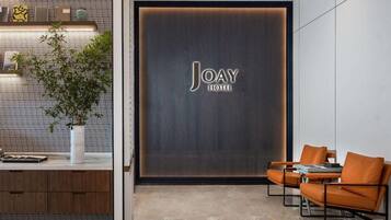A modern hotel lobby with a reception desk, seating area, and a large wall with the hotel name.
