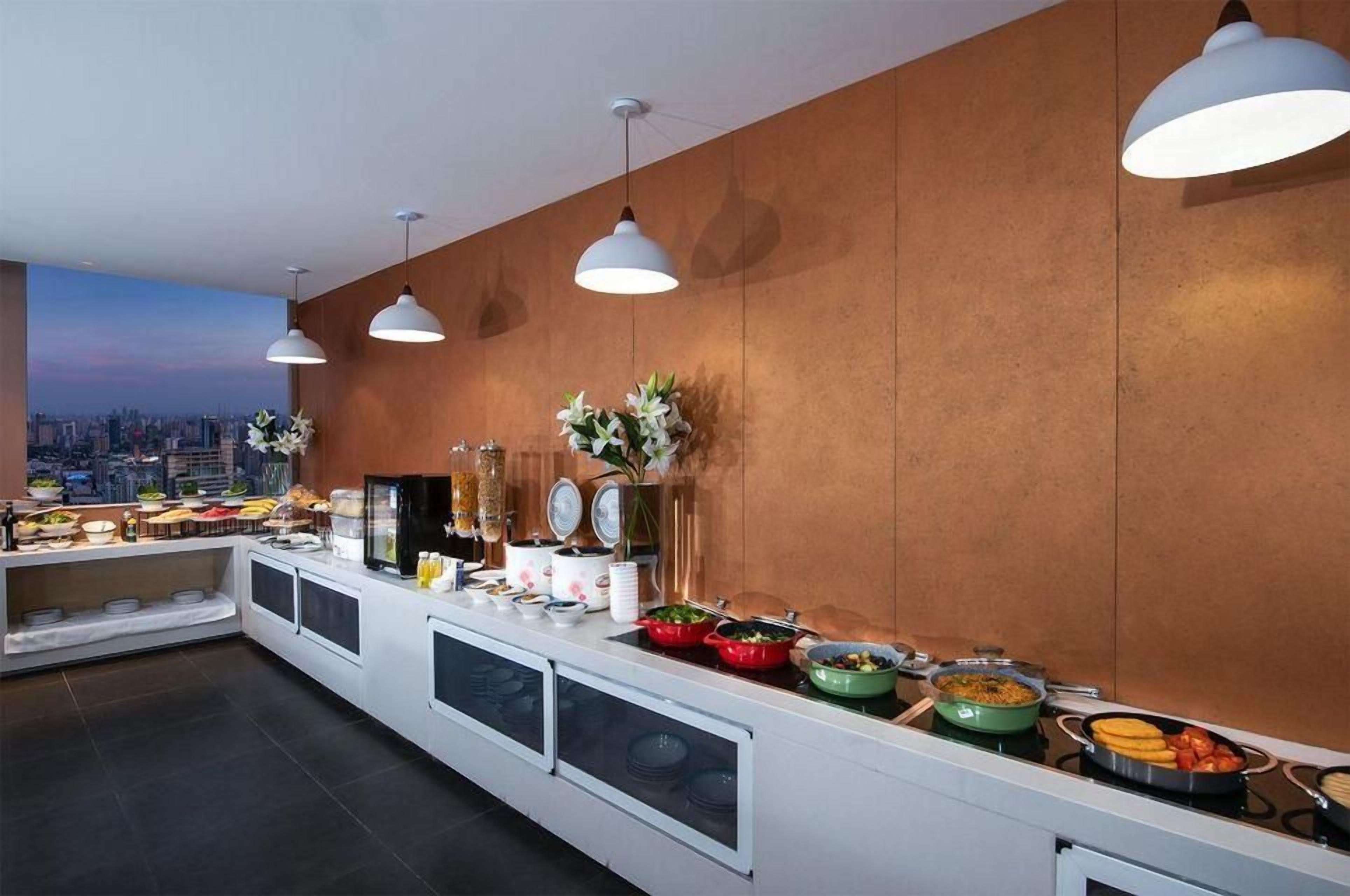 A buffet setup with various food items, a city view, and pendant lighting.