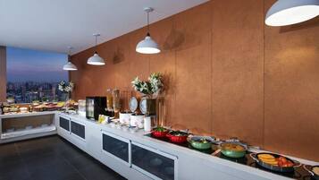 A buffet setup with various food items, a city view, and pendant lighting.