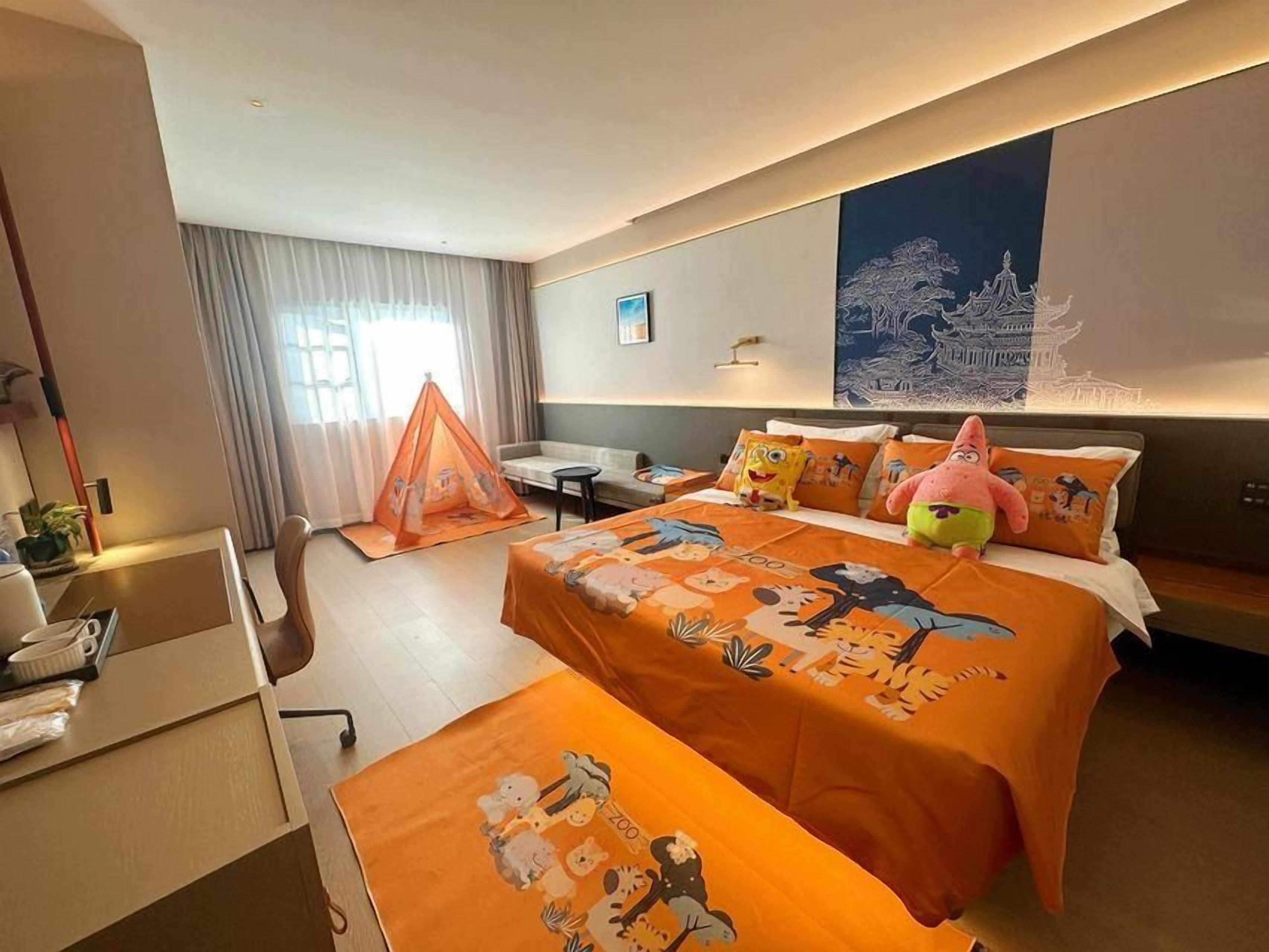 A hotel room with a bed, a desk, a chair, a small table, and a window with curtains.